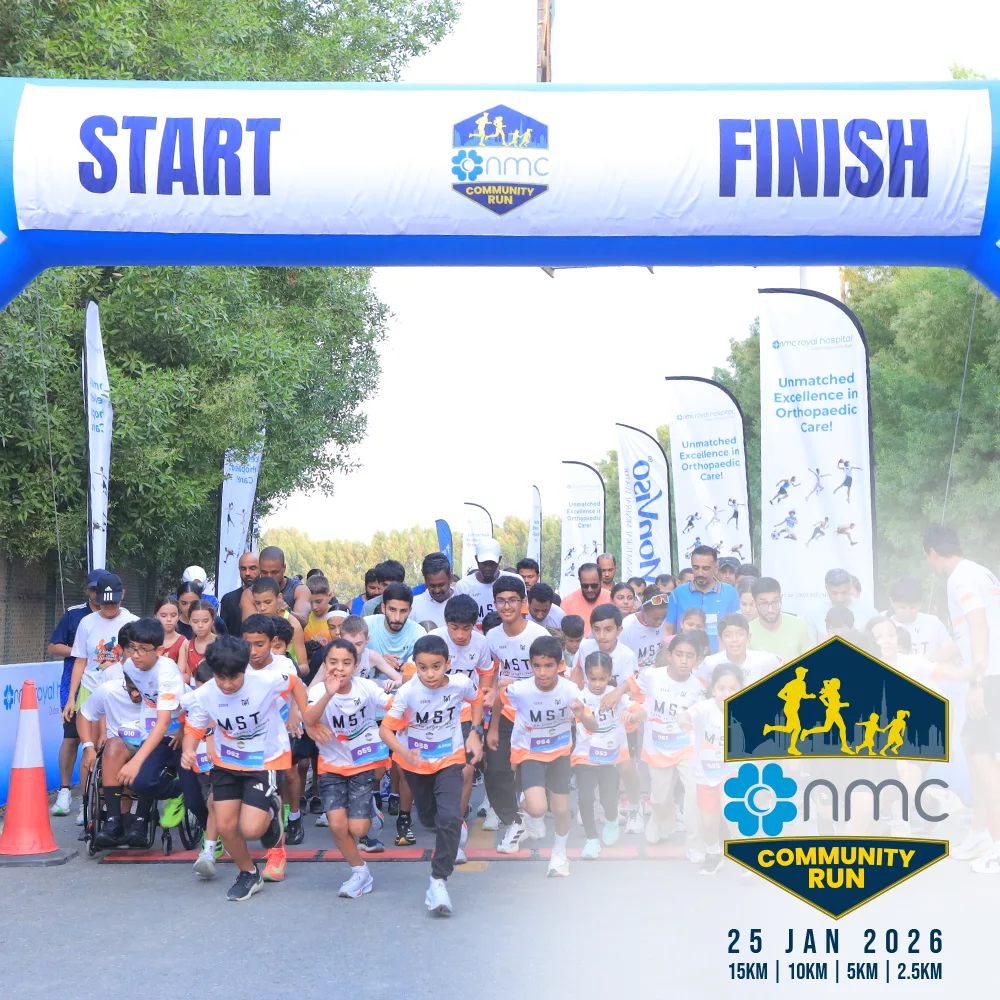 Participants sprint towards the start line of the NMC Community Run, with colorful banners and a scenic backdrop.