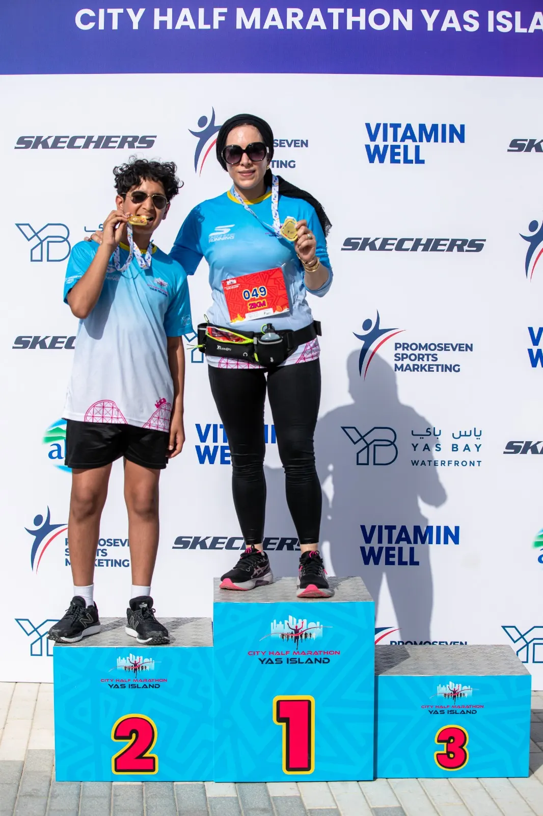 Two athletes celebrate their achievements on podiums at the City Half Marathon, displaying medals in front of a branded backdrop.