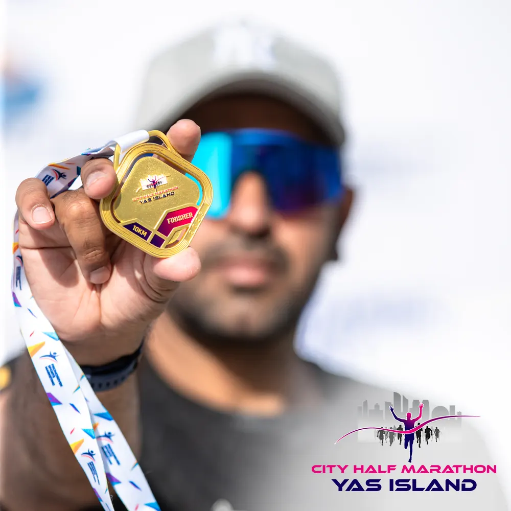 A person holds a gold medal with a colorful ribbon, celebrating their achievement at the City Half Marathon in Yas Island.