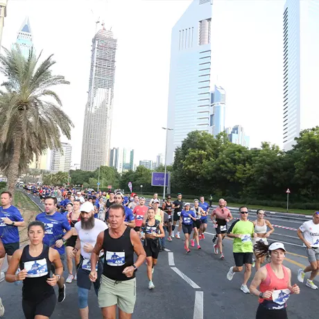 A diverse group of runners participating in an outdoor marathon, with modern skyscrapers and palm trees in the background
