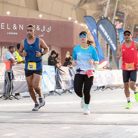 Runners compete in a race, surrounded by cheering spectators and event banners in an outdoor setting