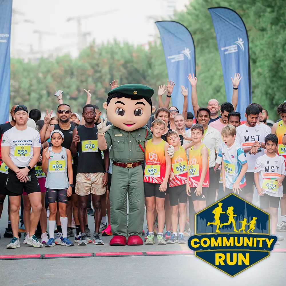 A diverse group of runners, some in colorful race shirts, pose with a mascot, celebrating the start of a community run event