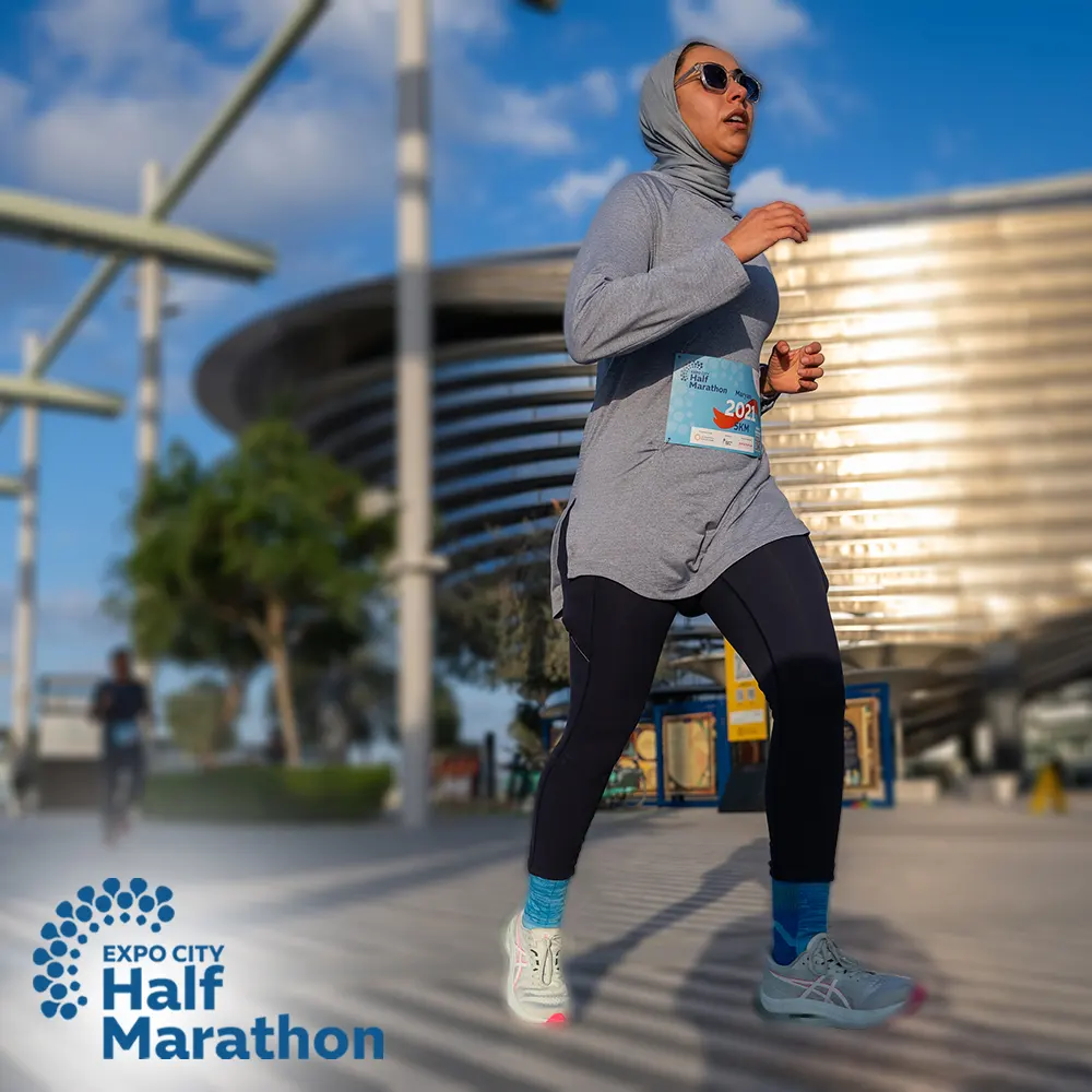 A female runner in athletic gear competing in the Expo City Half Marathon, with a modern building and blue sky in the background.