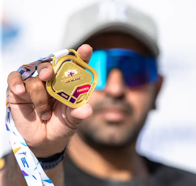 A person proudly holds up a gold medal with a colorful ribbon, celebrating a significant achievement in an outdoor setting.