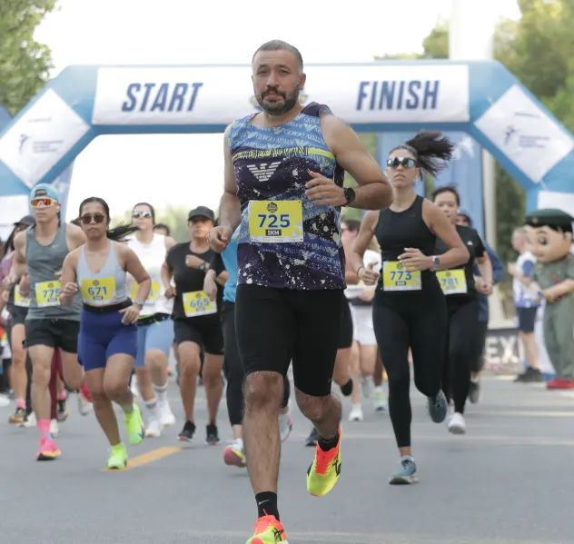 A diverse group of runners celebrating at a race start line, with many participants raising their hands in excitement under banners.