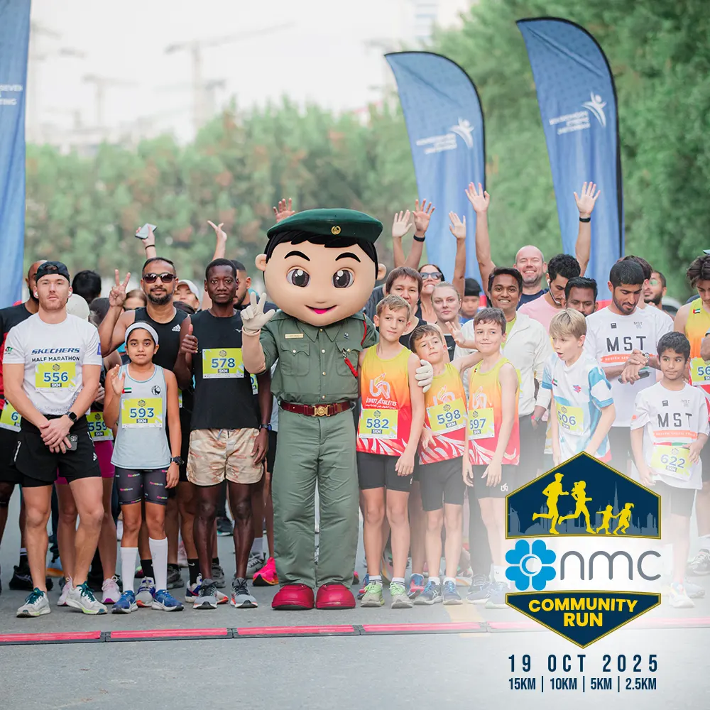A diverse group of participants, including runners of various ages, poses happily at a community run event with a mascot character.