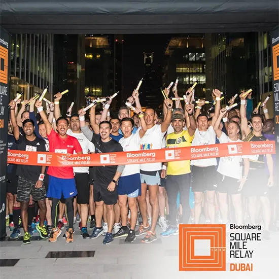 A group of athletes celebrating at the Bloomberg Square Mile Relay in Dubai, holding batons and posing together in a lively atmosphere.