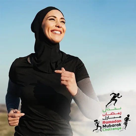 A woman jogs outdoors, wearing a black athletic top with a hijab, against a scenic backdrop, promoting the Ramadan Mubarak Challenge.