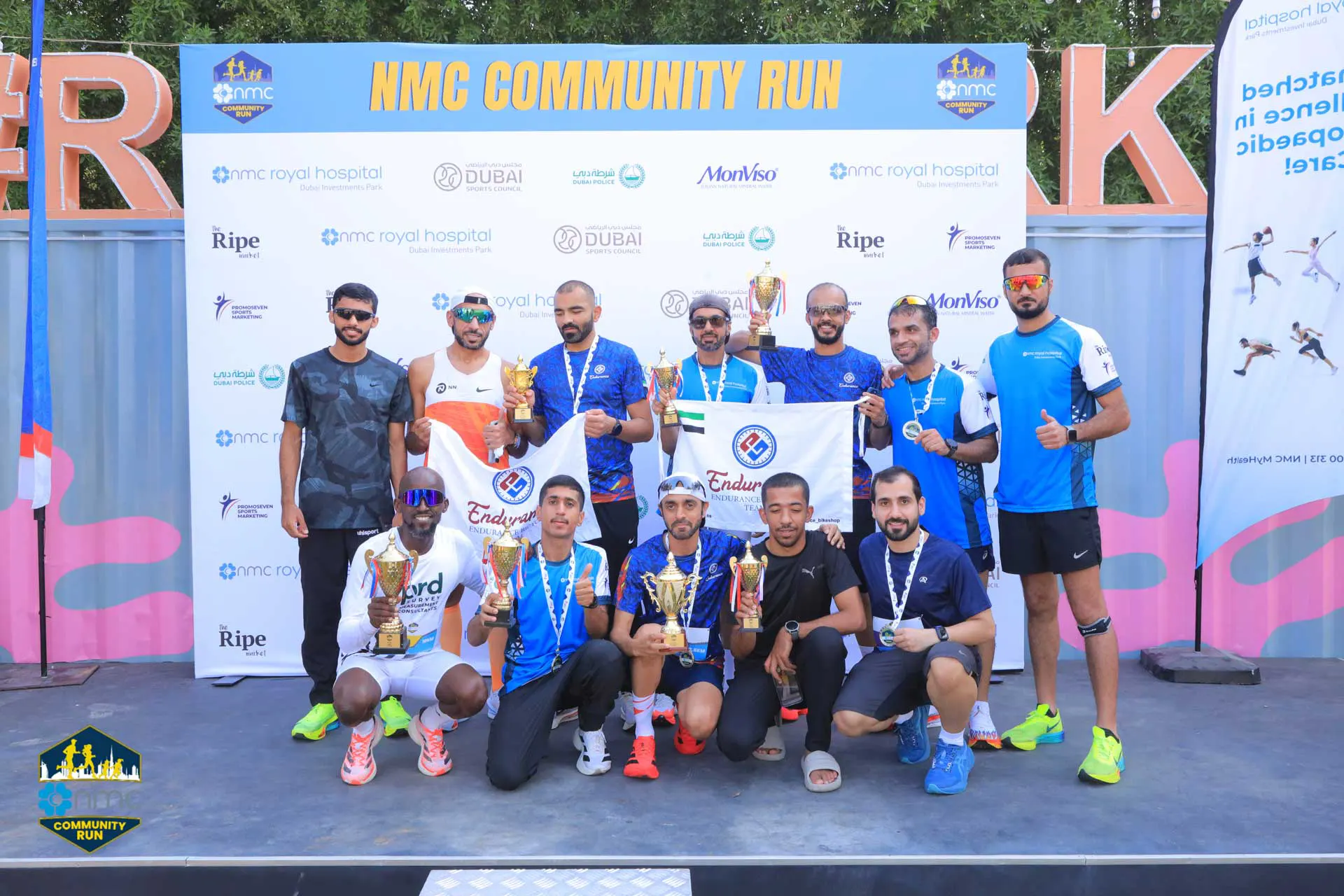 A group of athletes poses on stage with trophies after the NMC Community Run, showcasing team spirit and celebration.