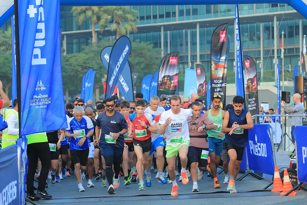 Runners start the Plus500 City Half Marathon in Dubai, surrounded by vibrant banners and cheering spectators.