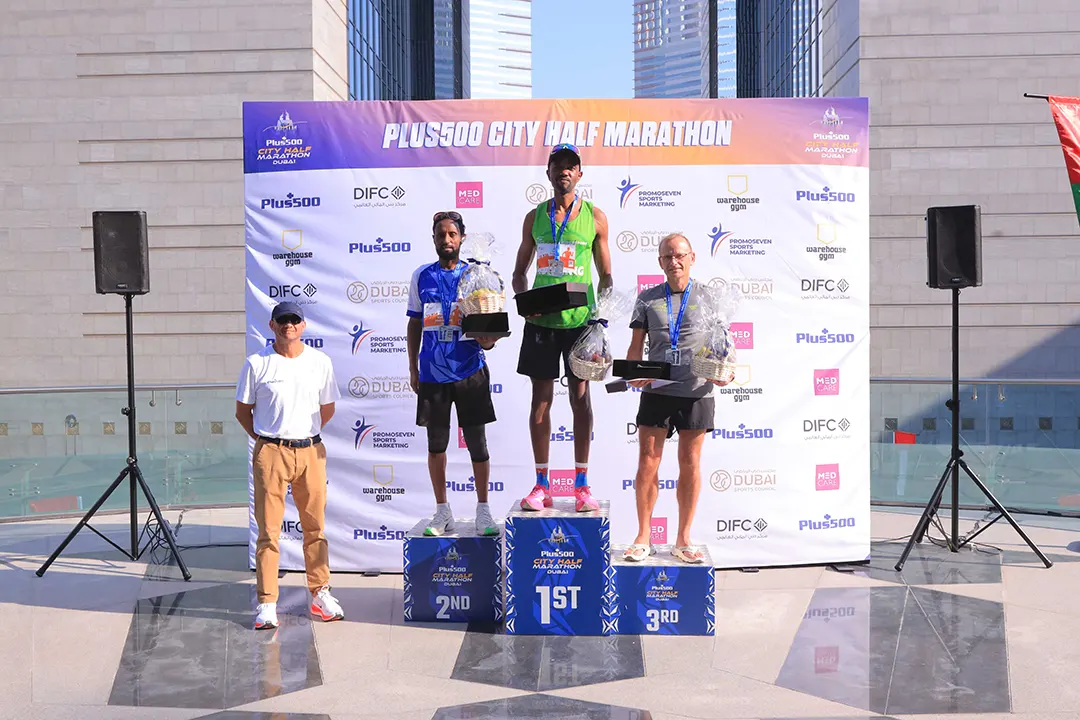 Winners of the Plus500 City Half Marathon stand proudly on the podium, holding trophies amid a vibrant event backdrop.
