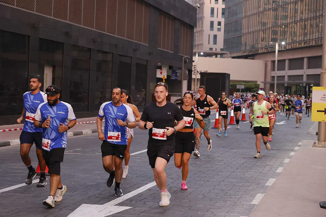 A group of runners in athletic gear participate in an outdoor race on a city street, surrounded by modern buildings.