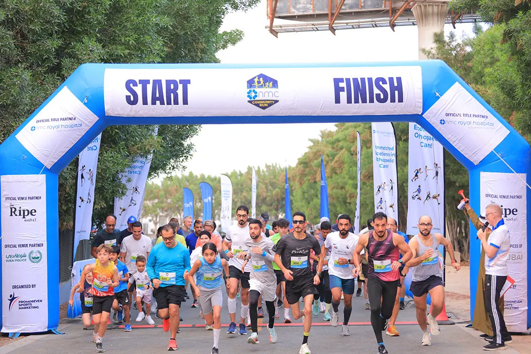 Runners sprint under a large inflatable arch marked START and FINISH, surrounded by banners at a community running event.