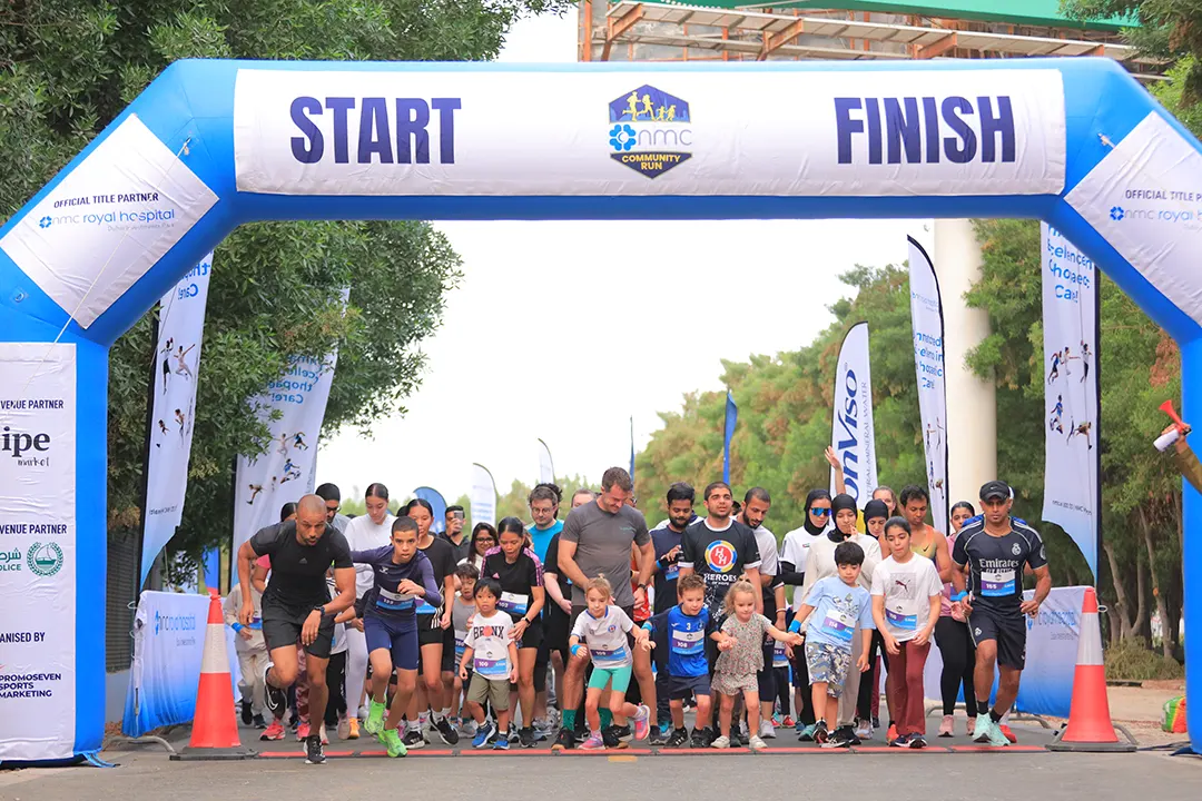 A group of runners, including children and adults, enthusiastically starting a community race under a Start and Finish arch.