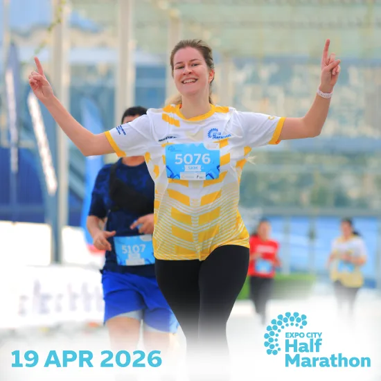 A runner in a yellow and white shirt holds up two fingers, celebrating during the Expo City Half Marathon on April 19, 2026.