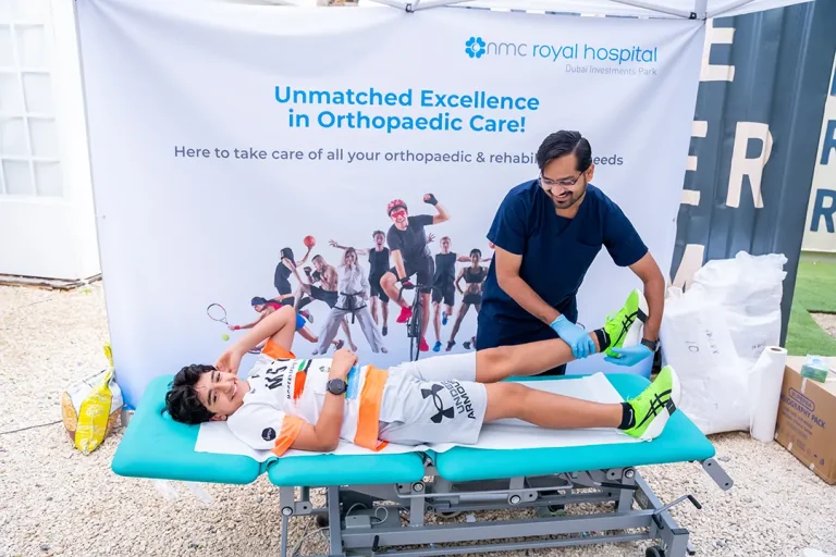 A therapist provides treatment to a young athlete on a therapy bed, with a banner promoting orthopaedic care in the background.