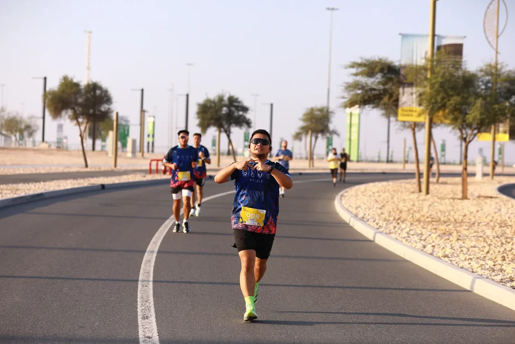 Runners participating in a marathon, wearing colorful shirts and bib numbers, jogging along a smooth, curved road lined with trees.