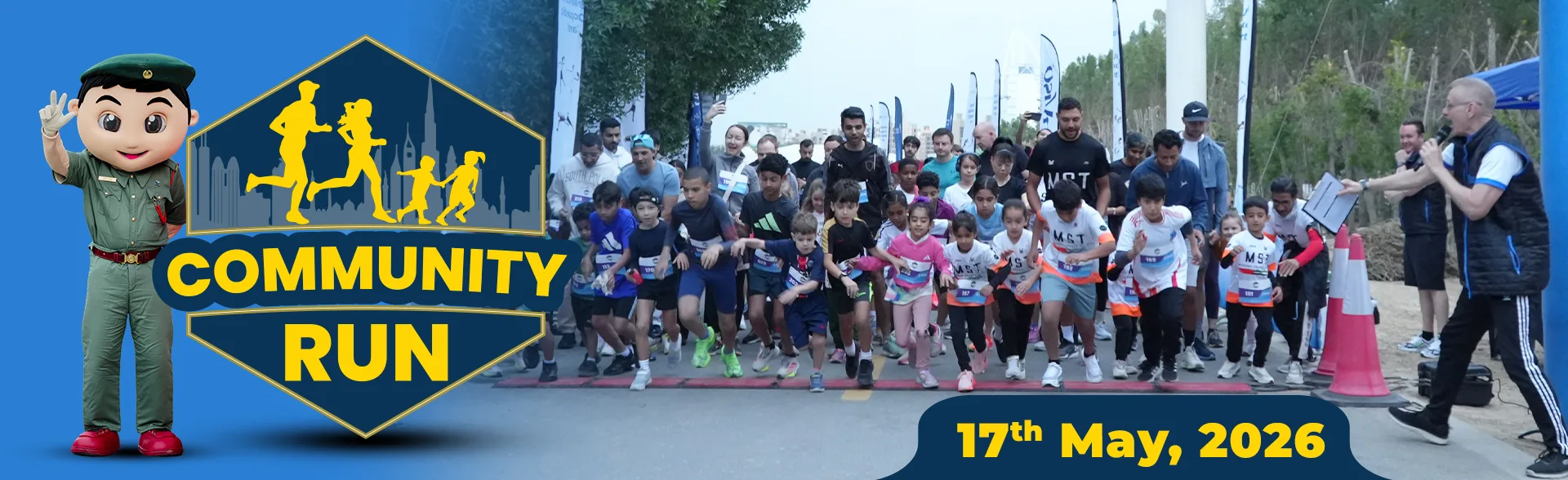Group of runners at the start line of a community run event on May 17, 2026, with a mascot and announcer on the sides.