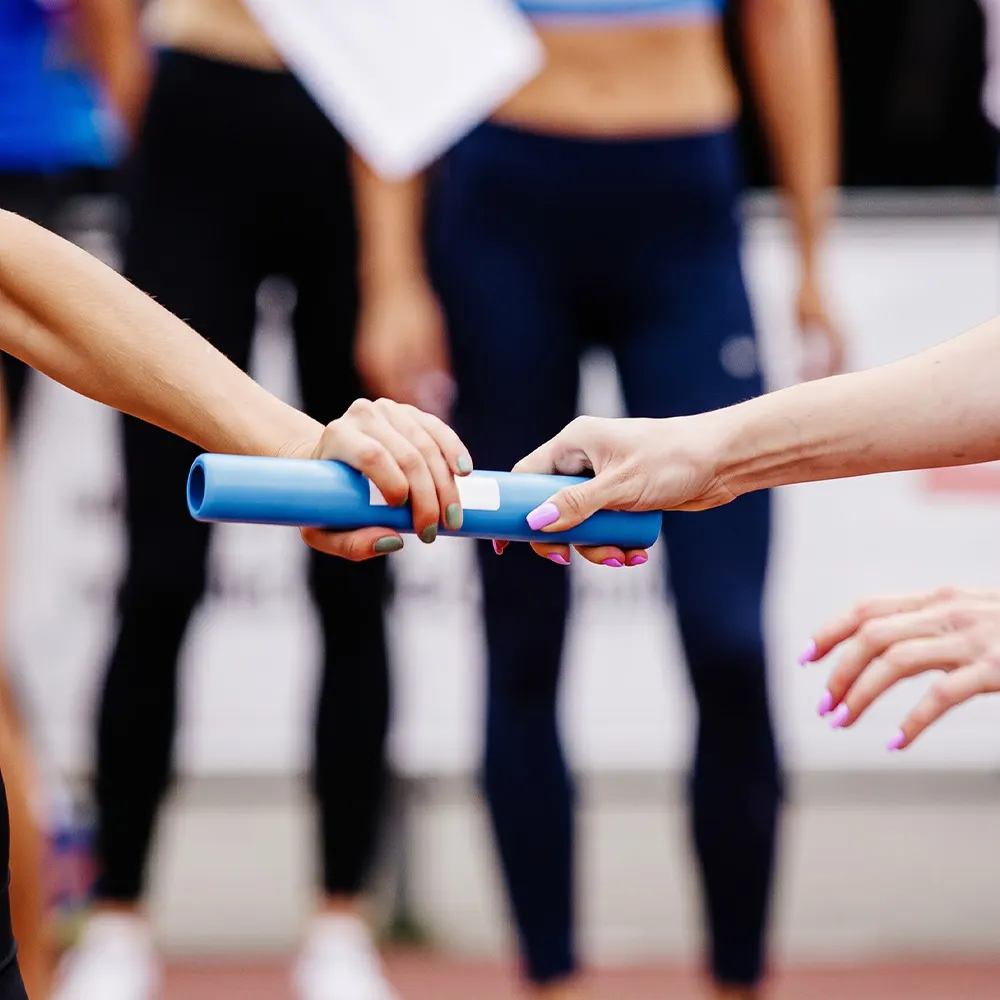 A group of runners celebrates at the finish line, holding relay batons and a ribbon that reads Bloomberg Square Mile Relay at night.