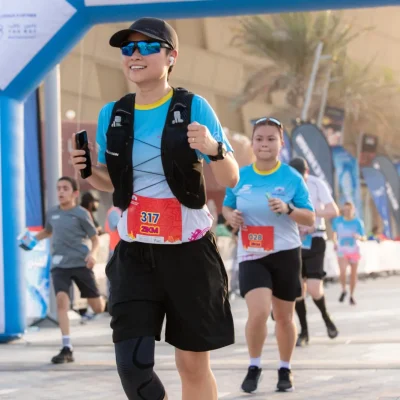 Runners participating in the City Half Marathon at Yas Island, passing under a blue START banner on a sunny day.